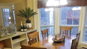 A dining area with a wooden table, chairs, a chandelier, and a large window with curtains. - HIdden Gem (Wallkill)
