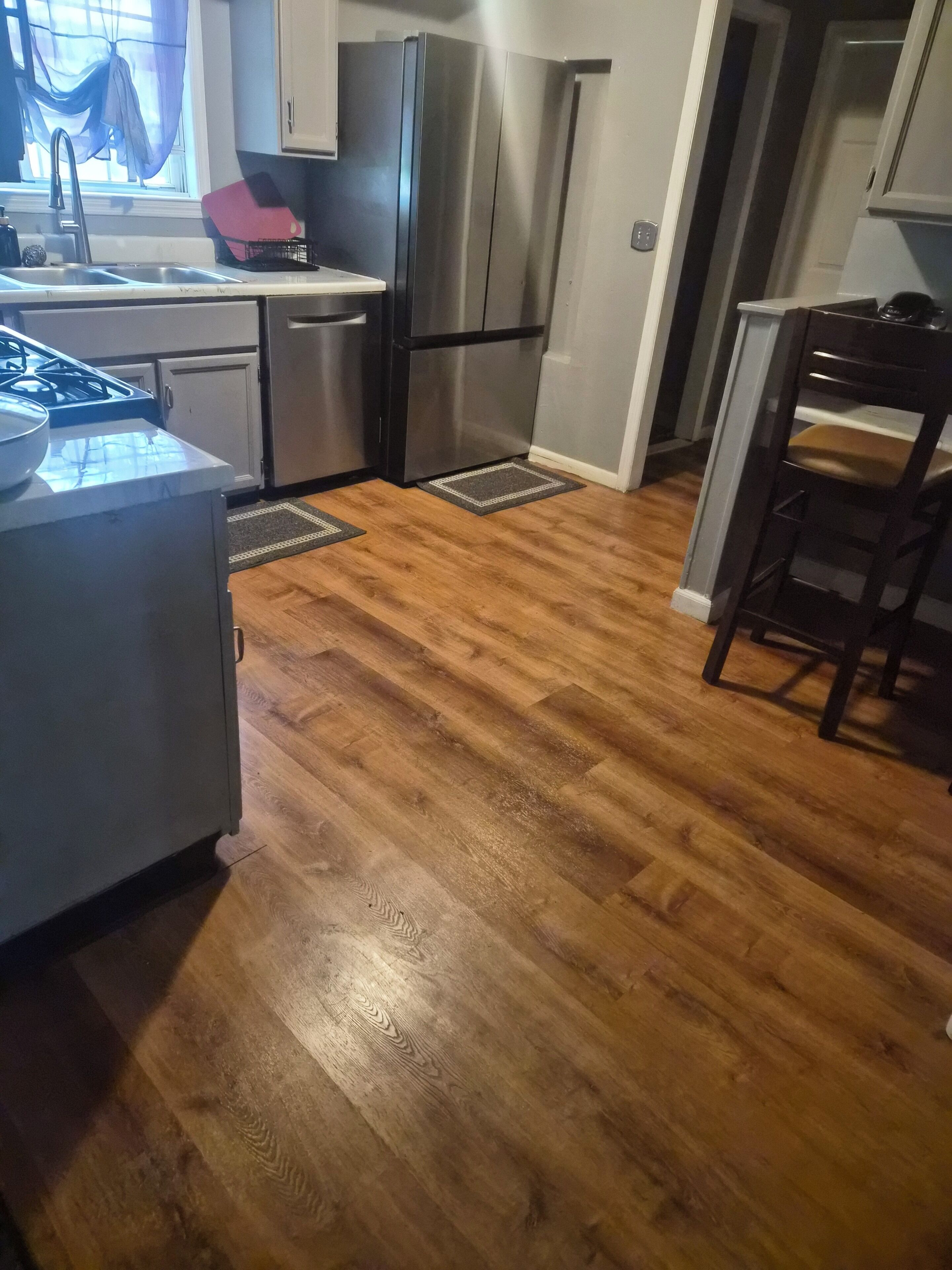Una cucina con frigorifero in acciaio inox, piano cottura a gas e pavimento in legno.
