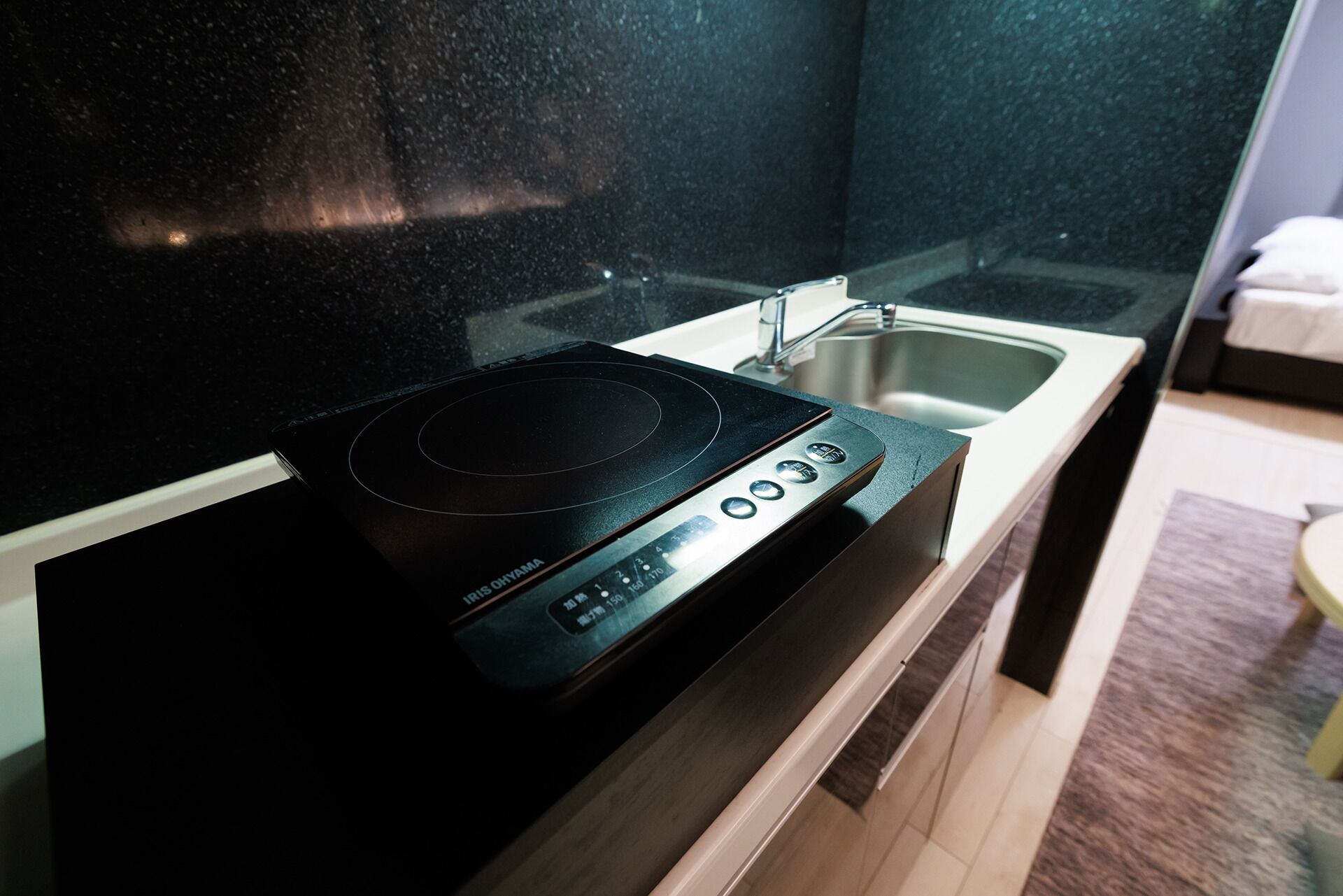 A kitchen with a black induction cooktop, a stainless steel sink, and a wooden cabinet.