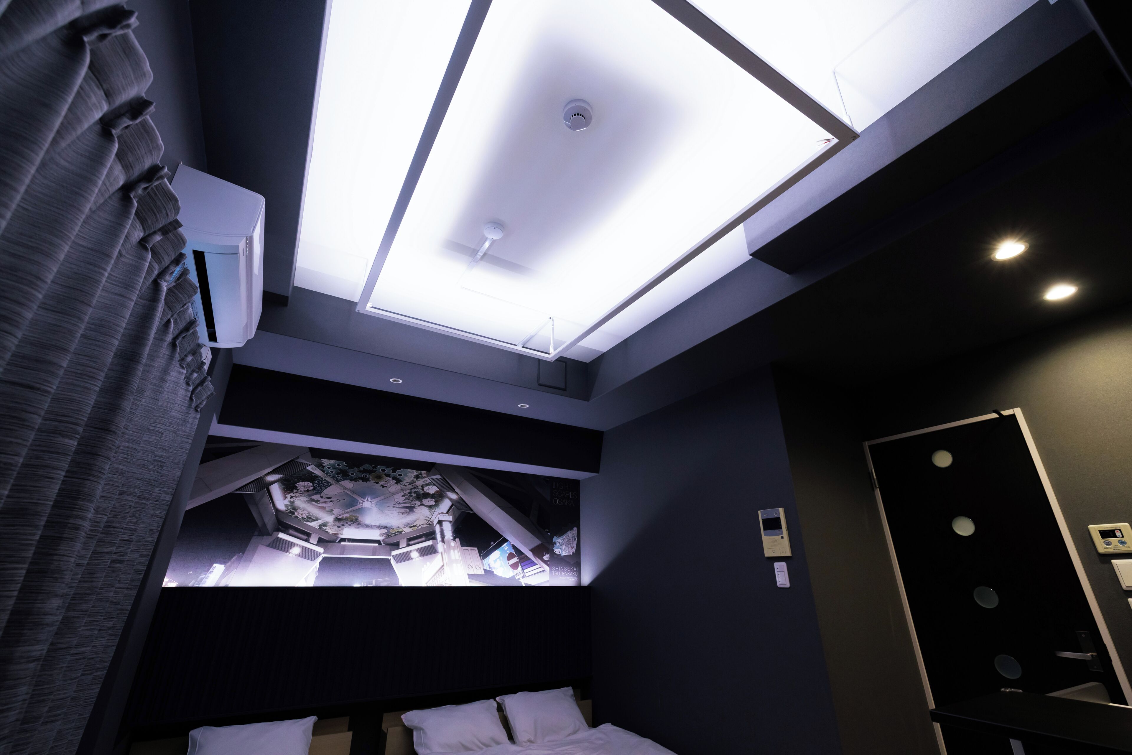 Una habitación de hotel moderna con tragaluz, una cama, una mesita de noche y un equipo de aire acondicionado de pared.