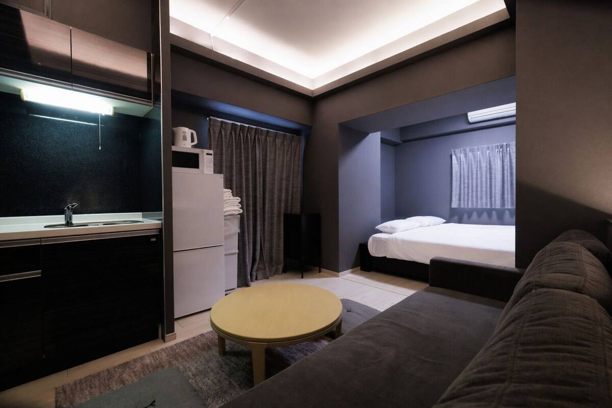 Habitación de hotel compacta con kitchenette, cama, mesa redonda y sofá.