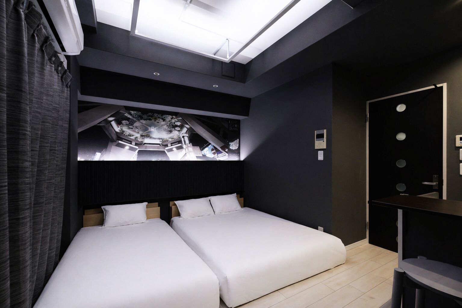 Ein modernes Hotelzimmer mit Dachfenster, zwei Betten, einer dunklen Wand und einem kleinen Schreibtisch.