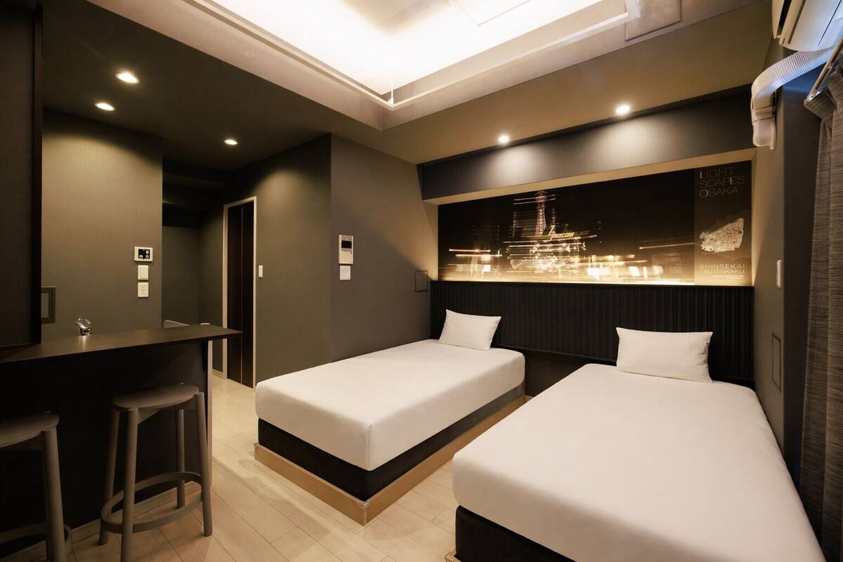 Una habitación de hotel con dos camas individuales, un escritorio con una silla y un minibar.