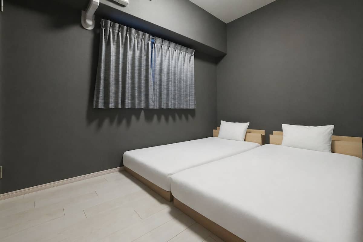 Un dormitorio con dos camas, una ventana con cortinas, una lámpara en el techo y suelo de madera.