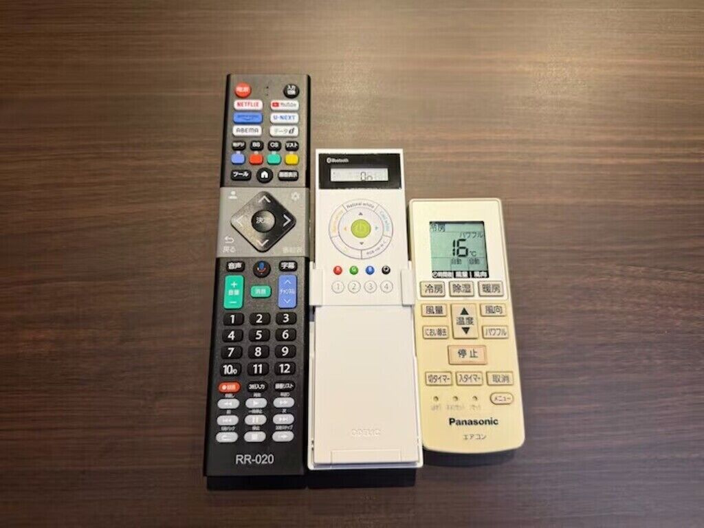 Une télécommande, un thermomètre numérique et un appareil Panasonic sur une surface en bois.