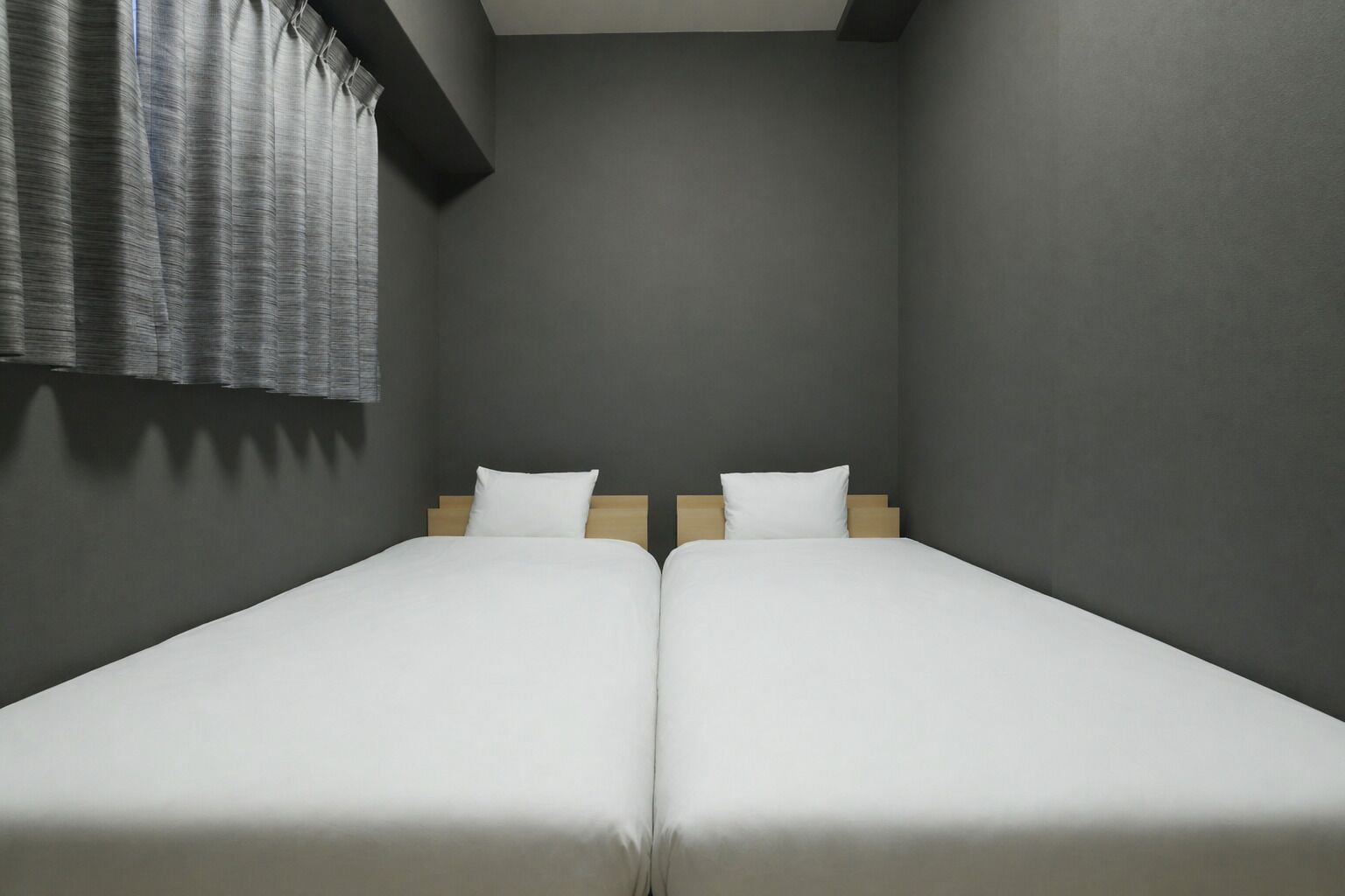 A room with two single beds, grey walls, and a window with curtains.
