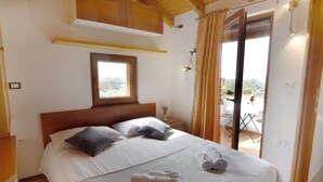 Una camera da letto con un letto, cuscini, una finestra, un comodino, un asciugamano e una porta finestra per il balcone.