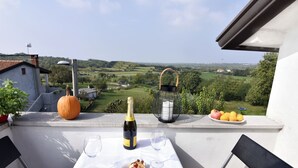 Un balcone con un tavolo apparecchiato per due persone, una bottiglia di champagne, un melograno e un piatto di arance.