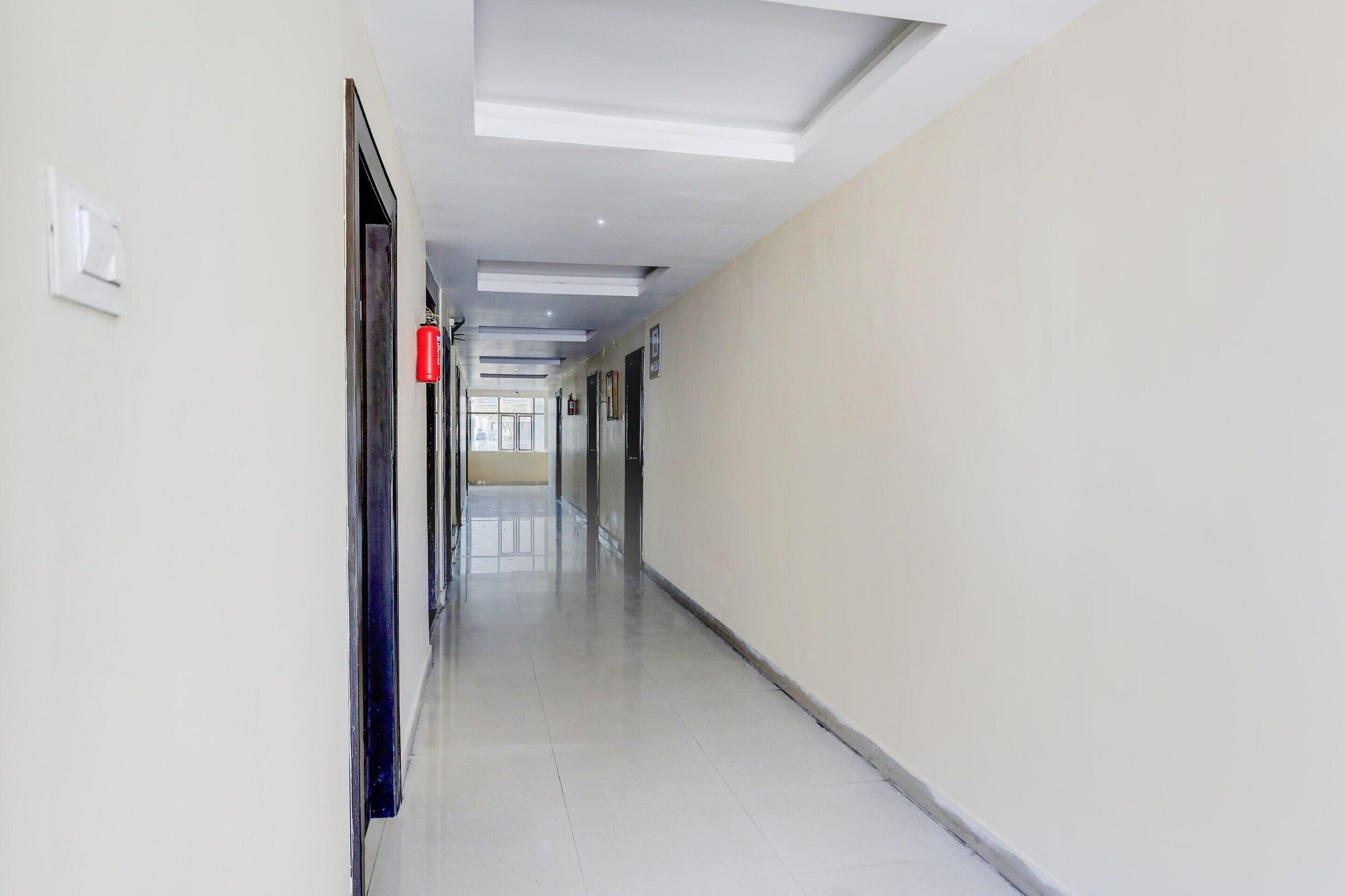 A long, narrow hallway with a ceiling light fixture, a fire extinguisher, and a door at the end.