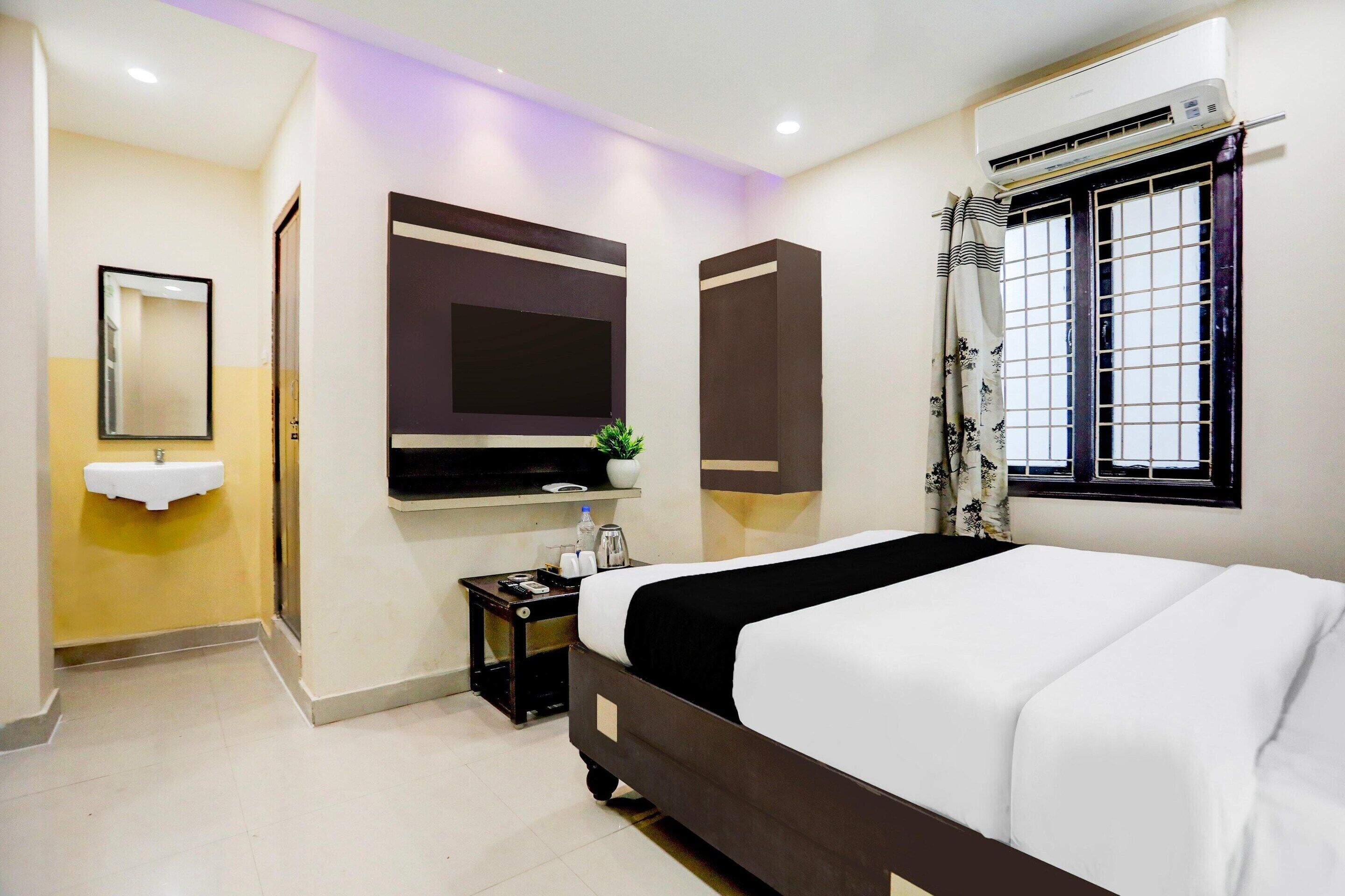 Une chambre d’hôtel équipée d’un lit, d’une télévision, d’une fenêtre avec des rideaux, d’un lavabo et d’un appareil de climatisation.