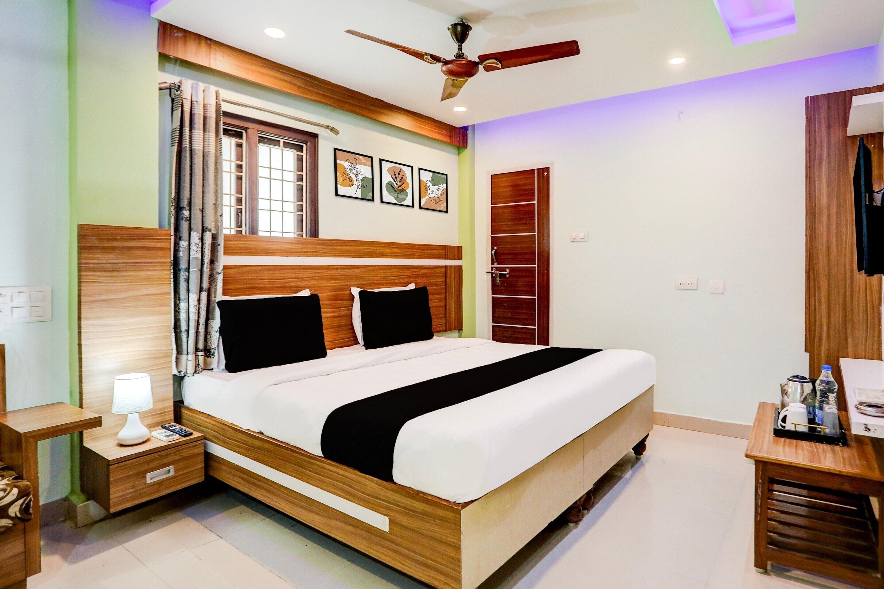 Une chambre d’hôtel avec un lit en bois, une table de chevet avec une lampe, un ventilateur de plafond et une armoire.