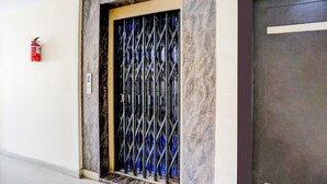 A door with a metal security gate, a fire extinguisher on the wall, and a marble-like textured wall. - Premium Sanjeevi Residency (Rajahmundry)