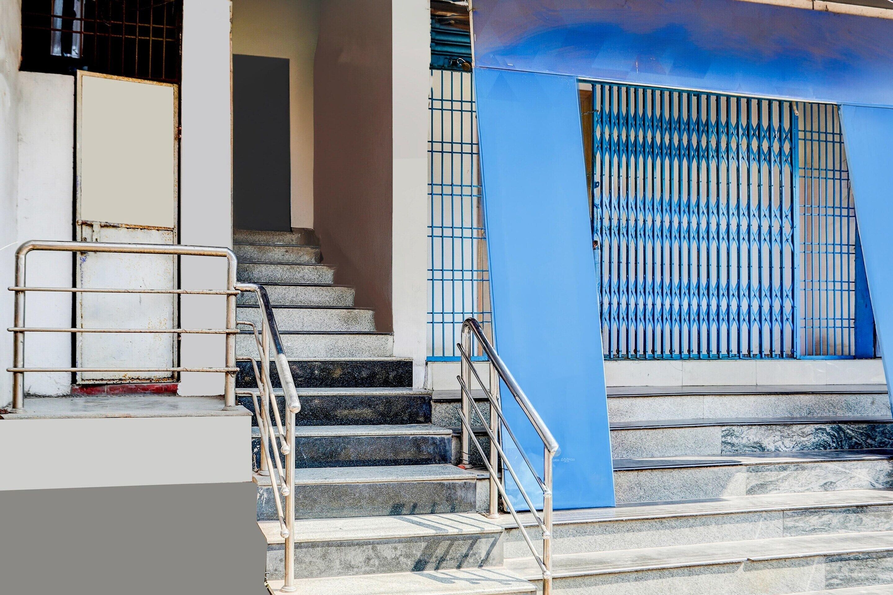 Un escalier menant à l’entrée d’un immeuble, avec des rampes en métal et une porte bleue dotée d’une grille métallique.