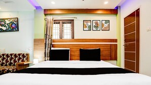 A hotel room with a large bed, a wooden headboard, a window with curtains, a wall-mounted artwork, and a door with a wooden panel. - Premium Sanjeevi Residency (Rajahmundry)