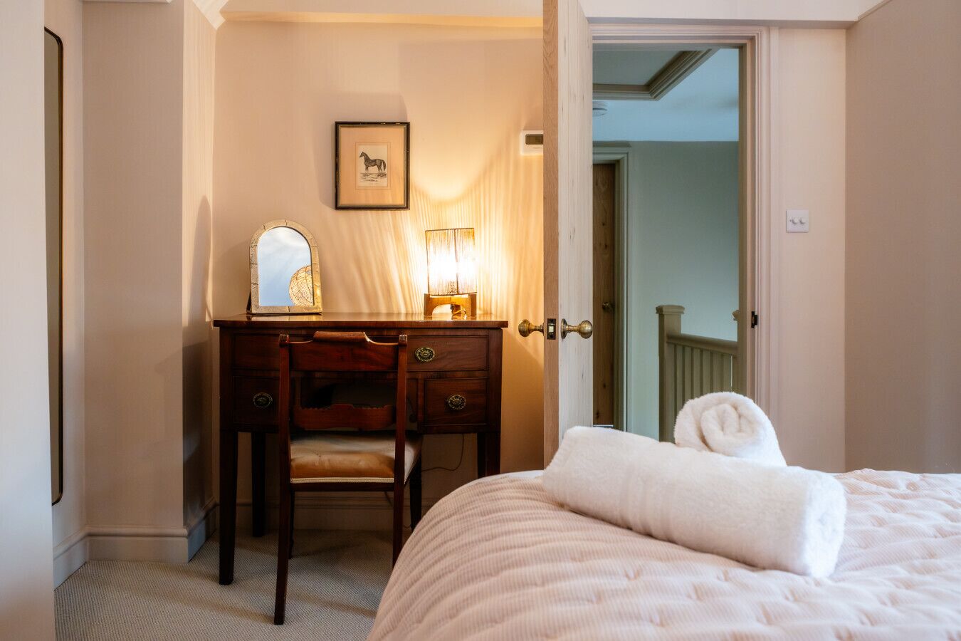 A bedroom with a bed, a wooden desk with a chair, a mirror, and a framed picture on the wall.