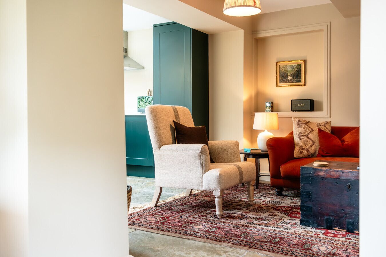 Une pièce avec une grande fenêtre, une chaise, un canapé rouge, une lampe et un tapis à motifs.