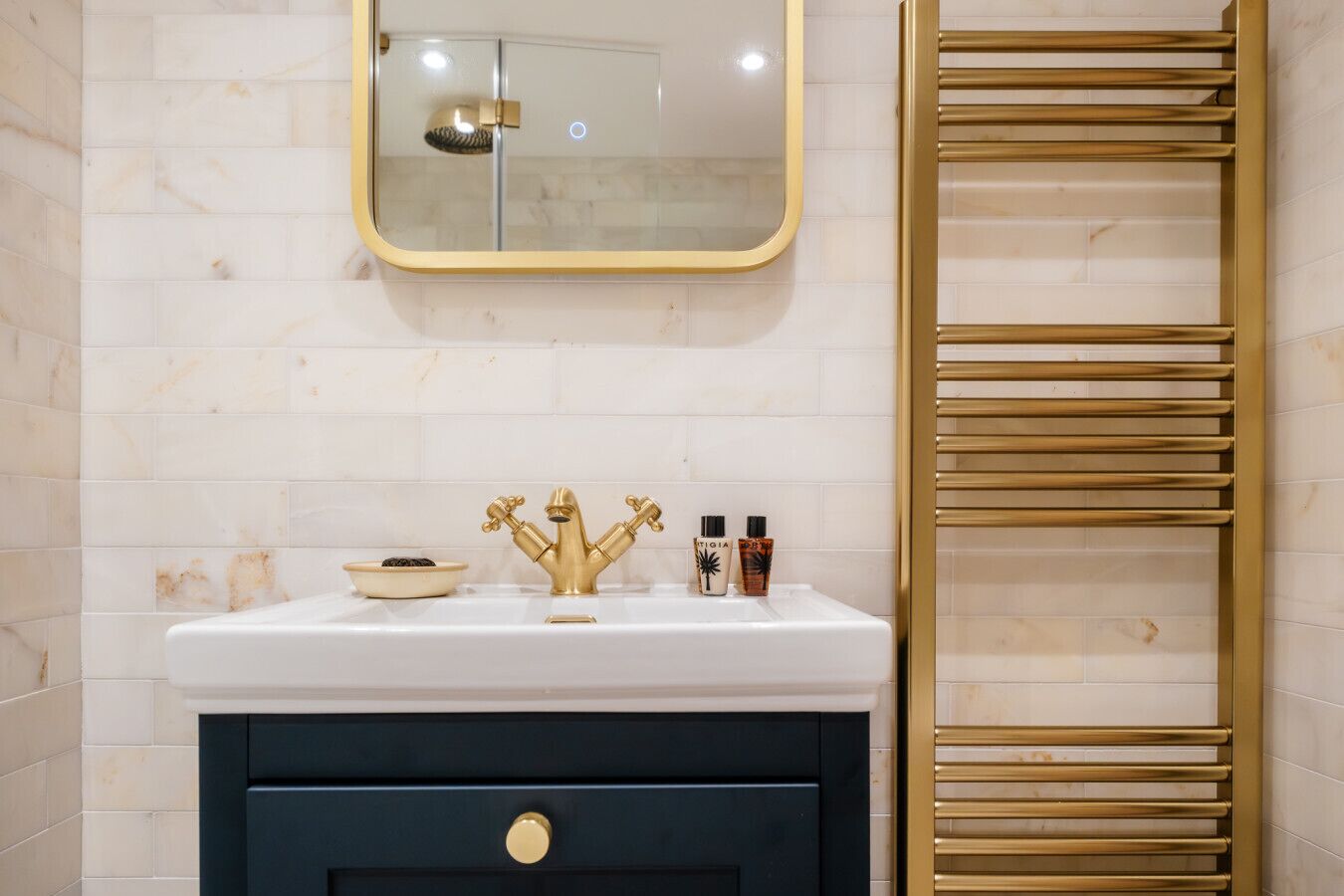 A bathroom with a white sink, gold faucets, a mirror, and a gold towel rack.
