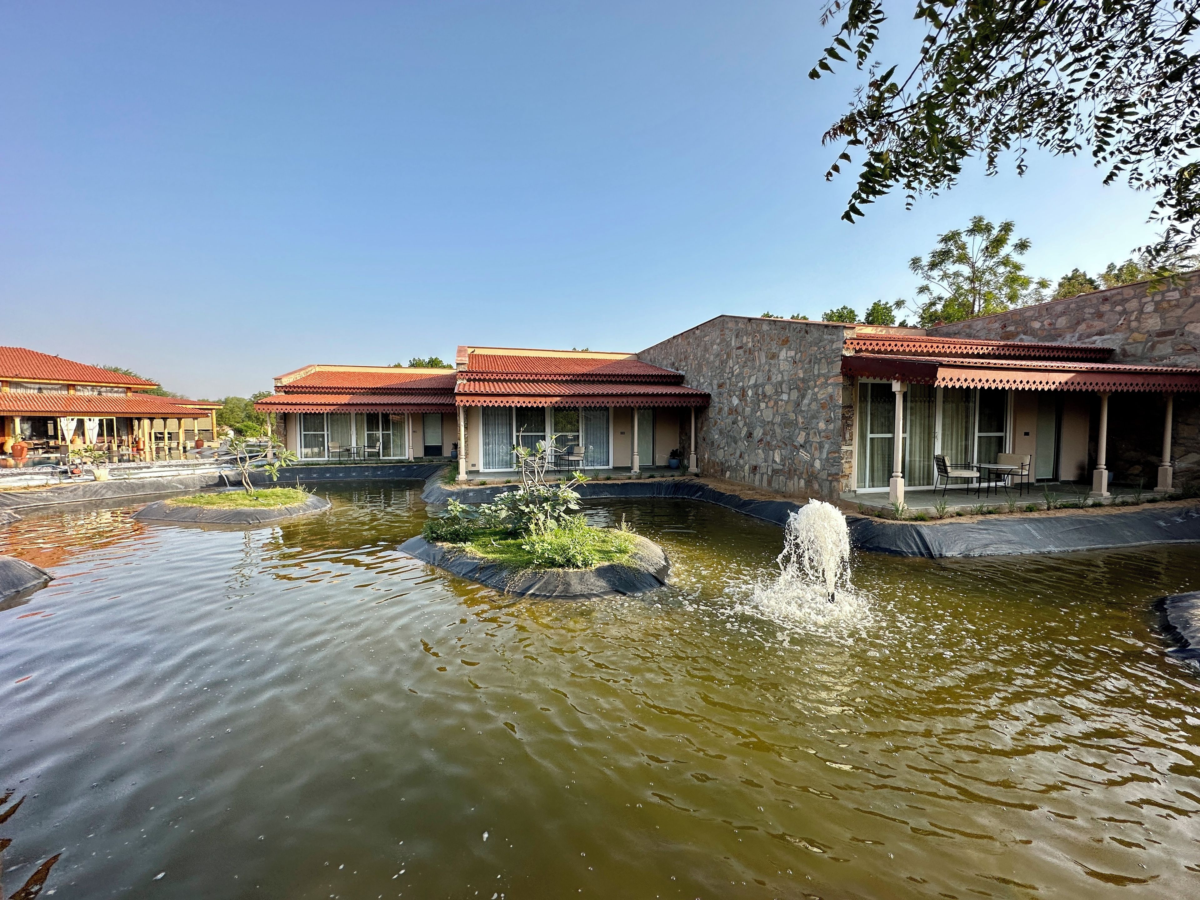 A hotel with multiple buildings, a pond with a fountain, and outdoor seating areas.