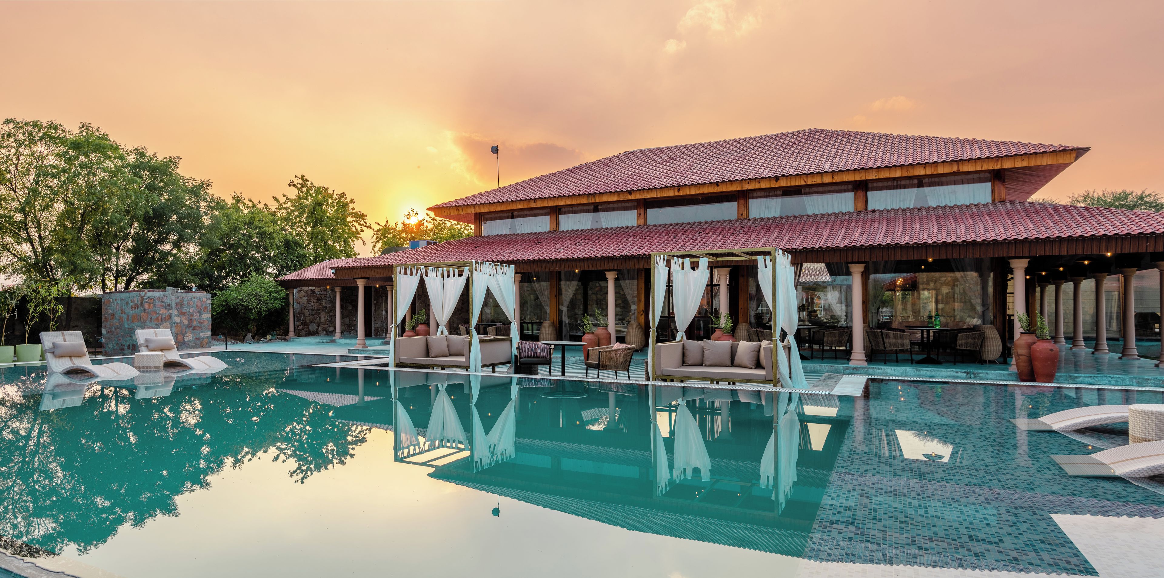 A resort with a large pool, outdoor seating, and a covered area with a view of the sunset.