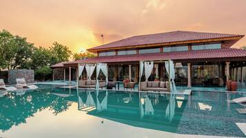 A resort with a large pool, outdoor seating, and a covered area with a view of the sunset.