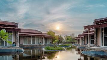 A traditional building with a pond in front, surrounded by greenery.