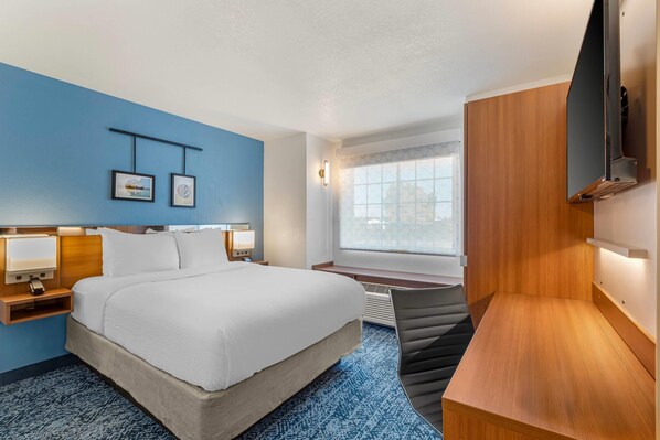 A hotel room with a large bed, bedside tables, a desk, a chair, a TV, and artwork on the wall.