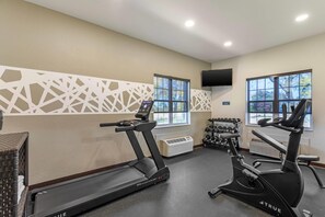 Un gimnasio con cintas de correr, una elíptica, un televisor montado en la pared y un estante con mancuernas.