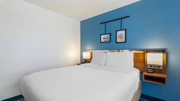 Una habitación de hotel con una cama grande, una mesita de noche con lámpara y dos cuadros en la pared.