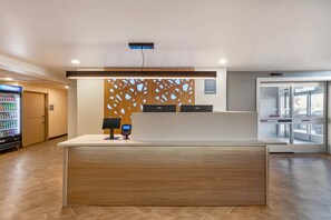 Mostrador de recepción de hotel con diseño moderno, una máquina expendedora y un acceso por puerta de vidrio.