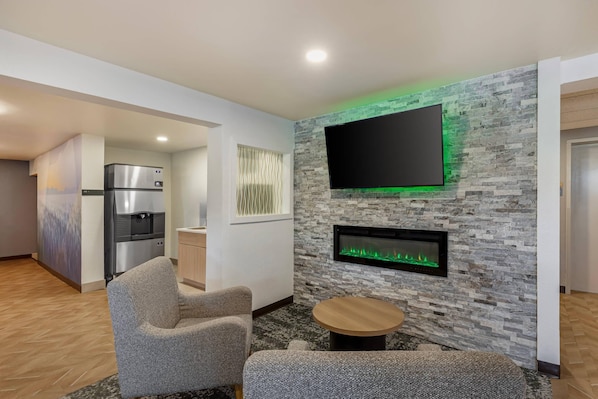 A modern living room with a flat-screen TV, a built-in fireplace, and a kitchen area with a refrigerator.