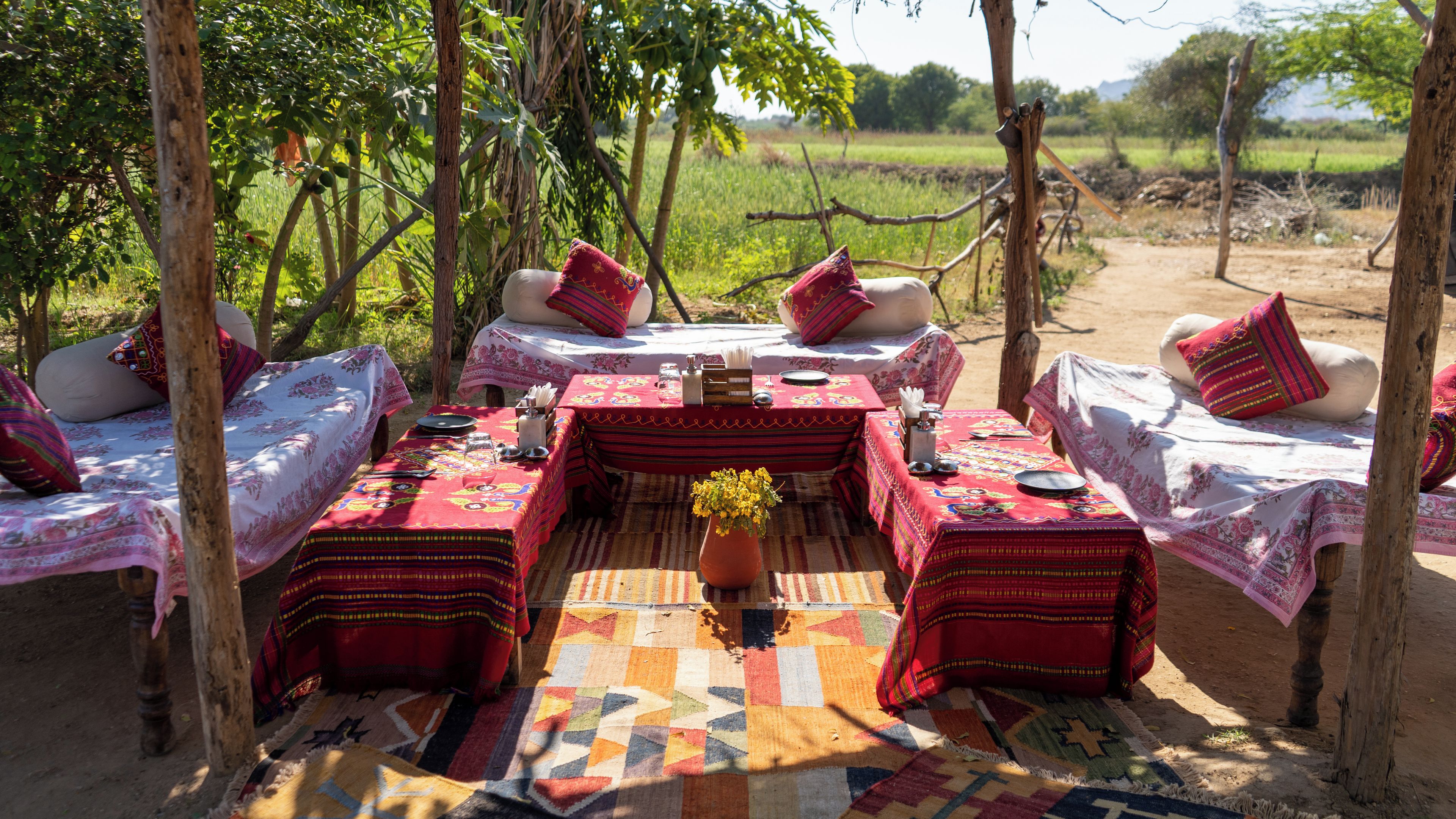 An outdoor dining area with tables set for two, surrounded by trees and a view of a field.