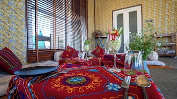 A dining table set with a patterned tablecloth, a glass of water, a glass of juice, and a plate with a spoon.
