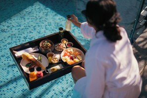 A tray with food and drinks, a person holding it, and a pool in the background. - Brij Pola,jawai (Bali)