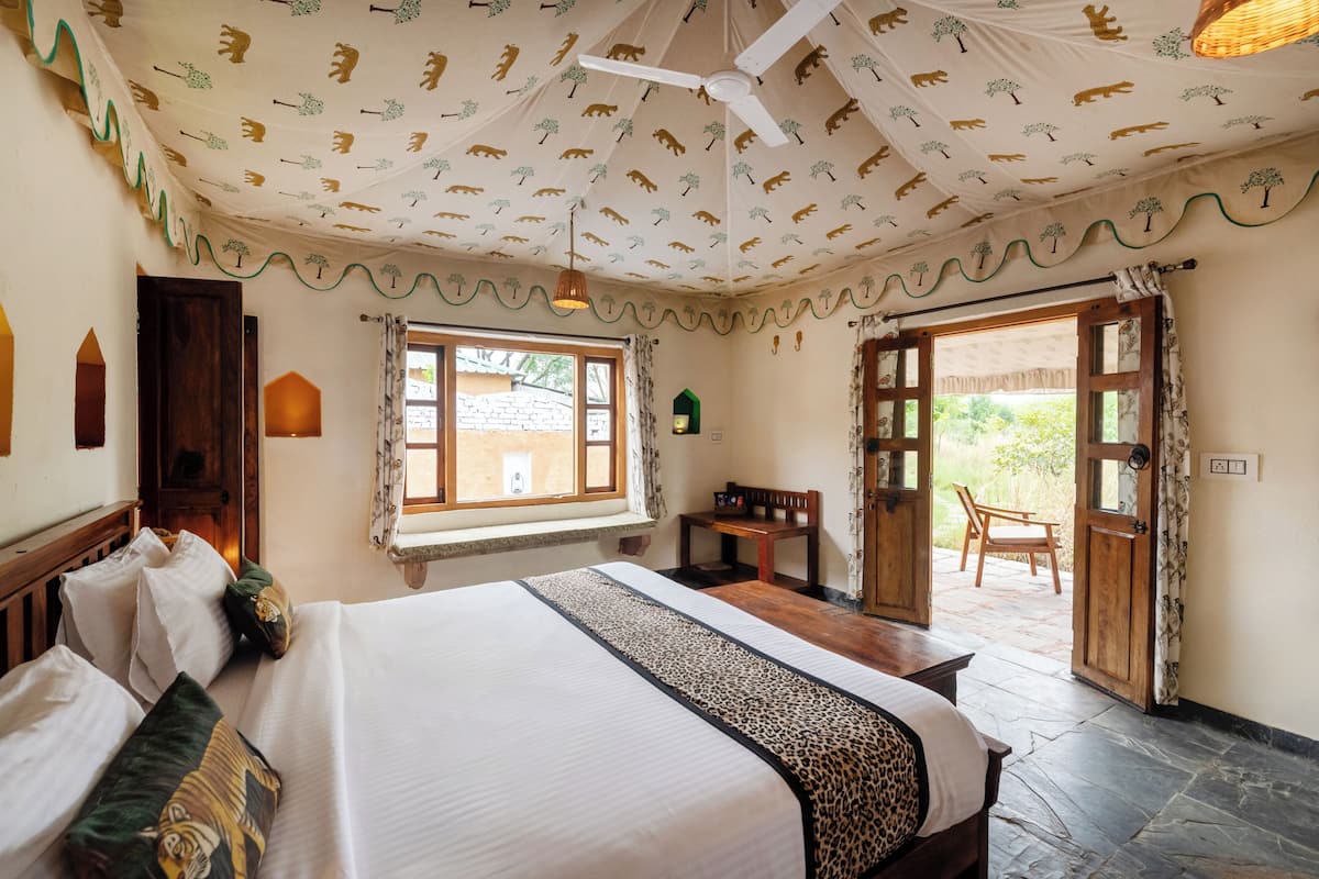 Un dormitorio con cama, escritorio y silla, una ventana y una puerta que da al exterior.