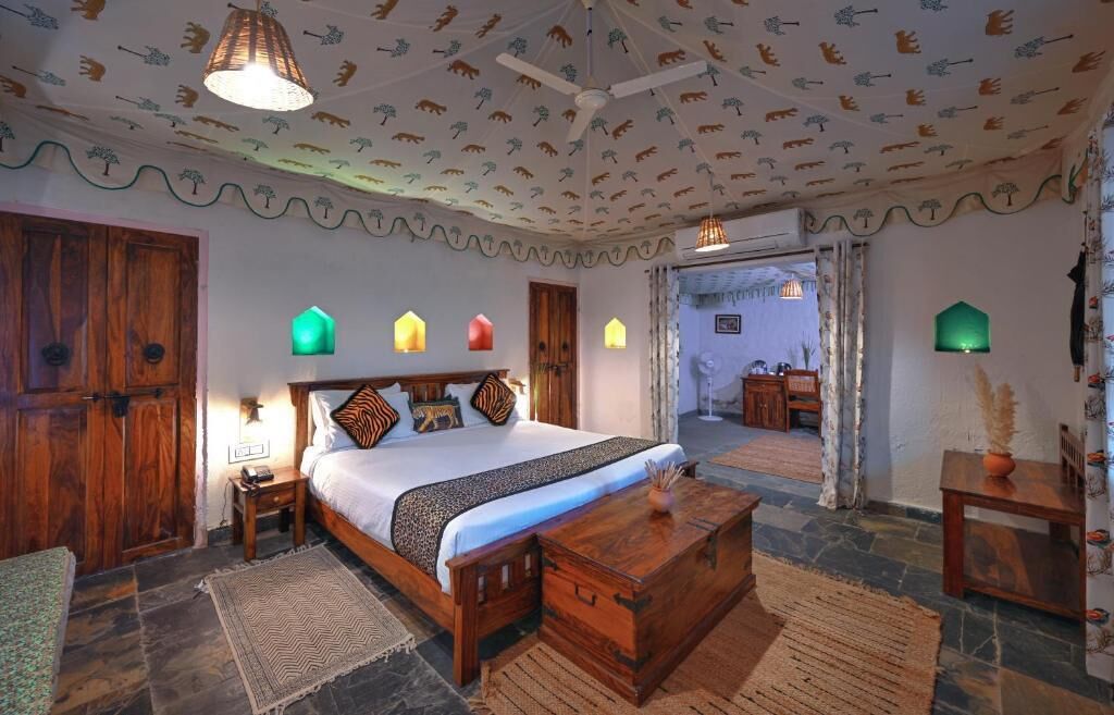 A room with a wooden bed, a nightstand, a wooden chest, a lamp, and a door leading to another room.