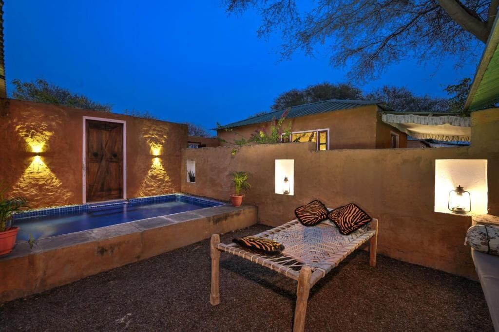 Un patio con piscina, un banco de madera y luces en la pared.