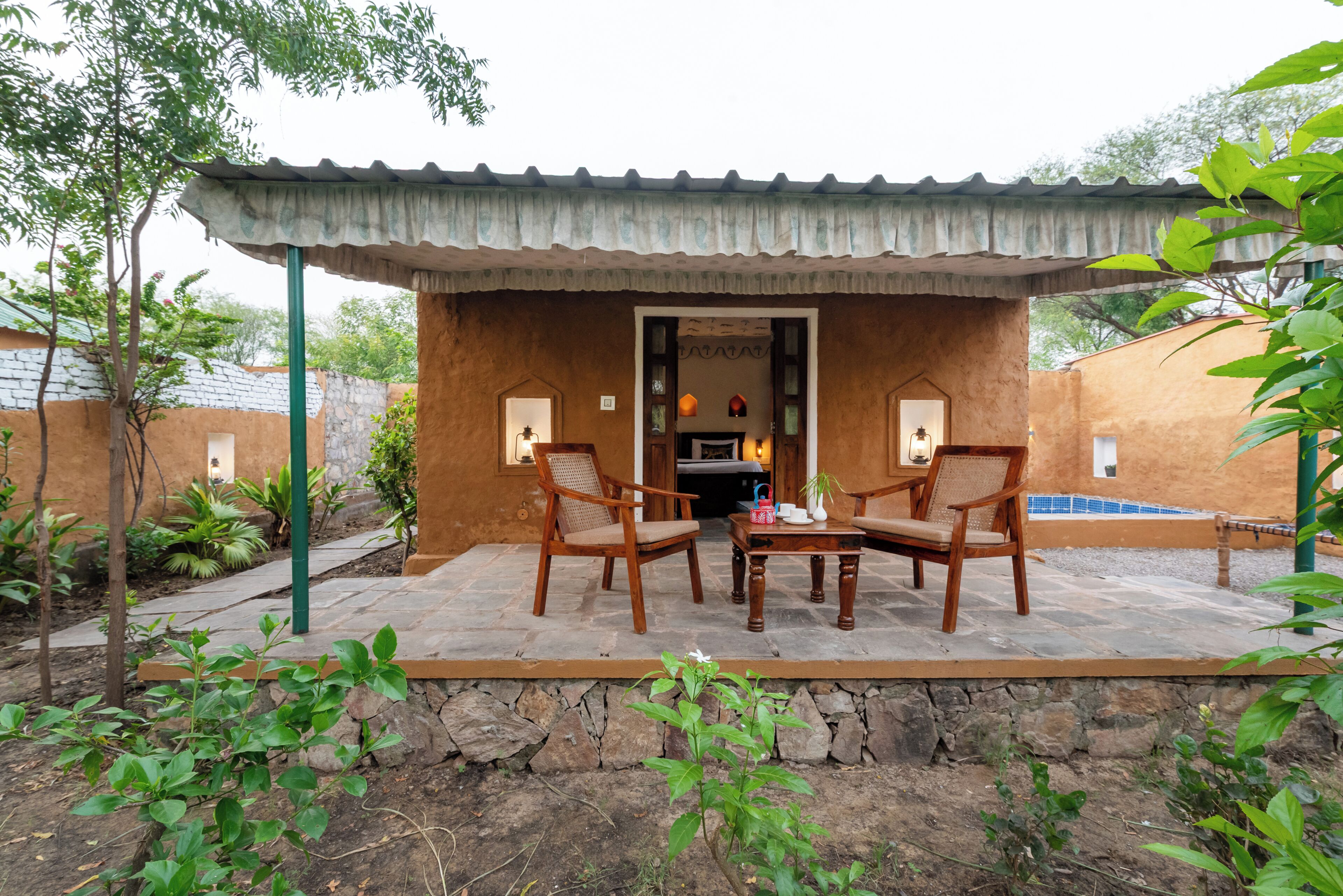 A patio with two wooden chairs and a table, a covered area with a tiled roof, and a stone wall.