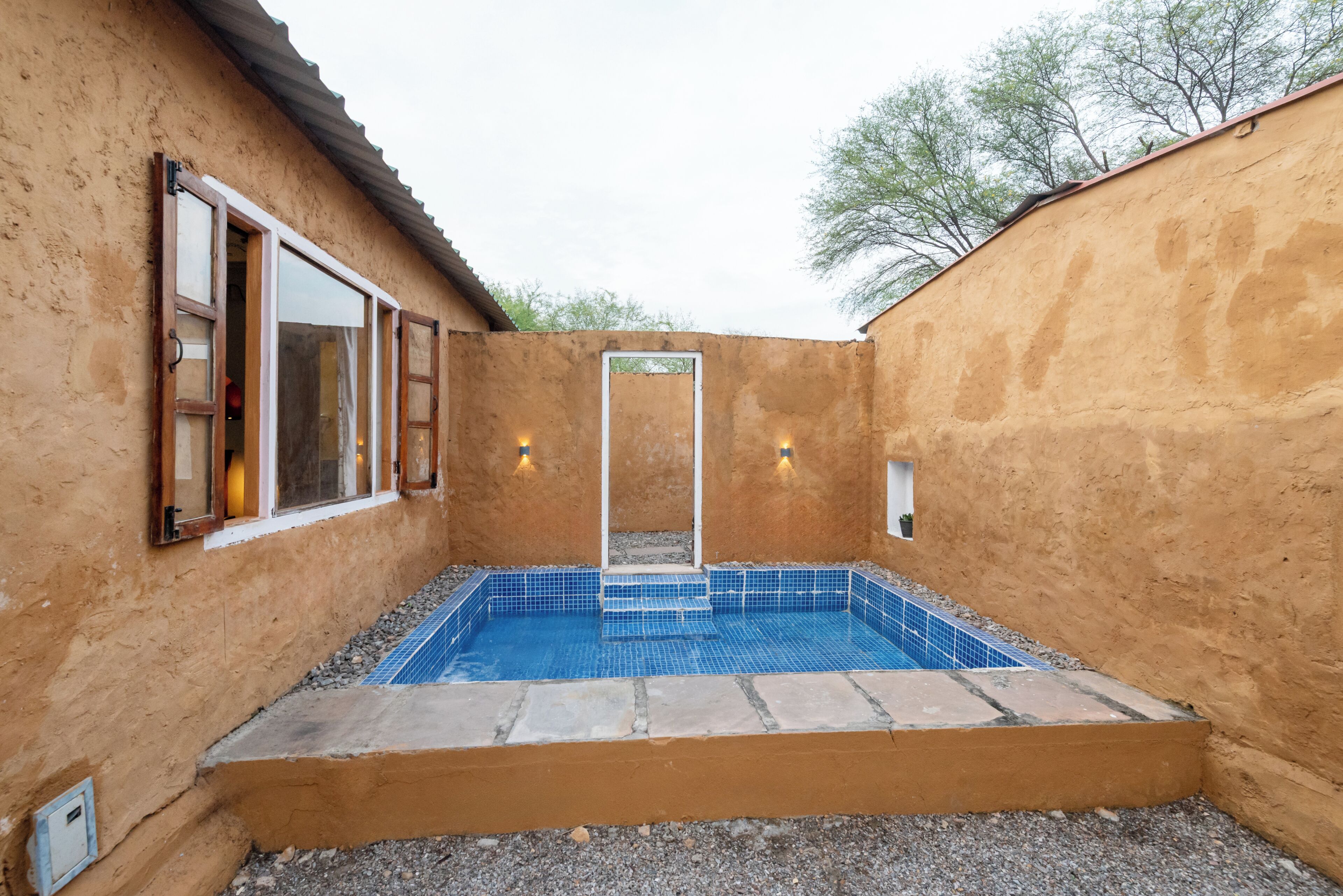 A swimming pool with a tiled deck, a door, and a window on a building with a textured wall.