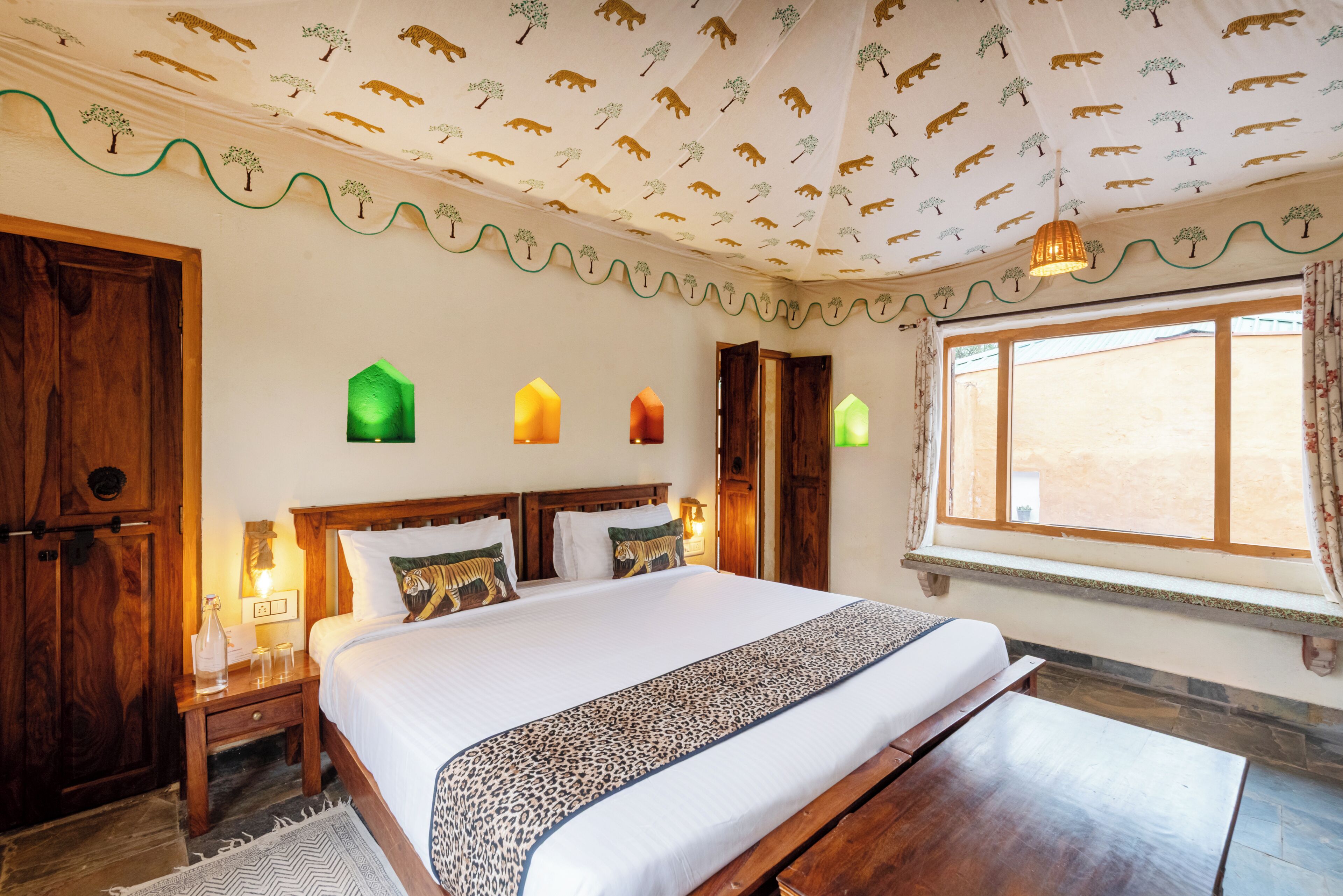 Une chambre à coucher avec un grand lit, une tête de lit en bois, des lampes de chevet, une fenêtre avec des rideaux et un plafond orné d’un motif représentant des ours.