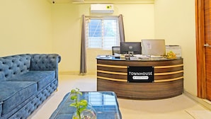 Un mostrador de recepción con la etiqueta 'Townhouse & Company Serviced', un sofá azul con textura y una mesa de centro de vidrio con una planta.