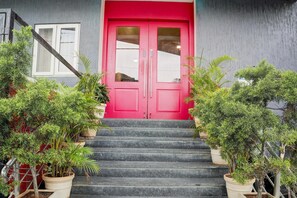 A red door with a glass panel, flanked by potted plants, leading to a staircase. - Super Townhouse Ulsoor Halasuru Station (Bengaluru)