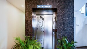 Un ascenseur orné d’une pancarte « BIENVENUE », d’un dessin fait à la main sur la porte et de pots de plantes de chaque côté.