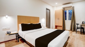 Une chambre d’hôtel comprenant un lit, une table de chevet, une lampe, une armoire et un bureau avec une chaise.