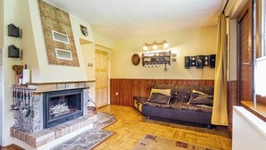 Un salon avec une cheminée, un plancher en bois, un canapé et une étagère fixée au mur.