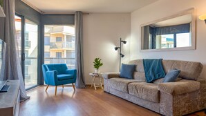 Una sala de estar moderna con un sofá, un sillón azul, una mesita auxiliar con una planta y un ventanal con cortinas.