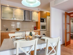 A modern kitchen with white cabinetry, a dining table set for four, and a visible washing machine. - Sedna: Apartment with sea views (L'Escala)