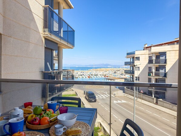 A balcony with a view of a marina, a table with breakfast items, and a clear sky. - Sedna: Apartment with sea views (L'Escala)