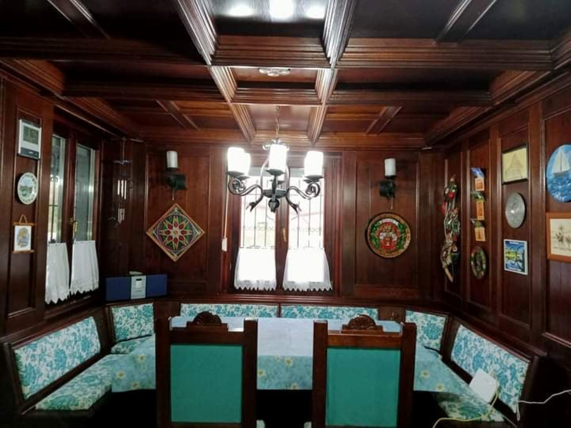 A room with wooden paneling, a chandelier, a bench with floral upholstery, and wall-mounted decorations.