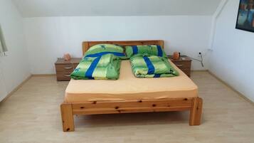 Een enkel bed met een houten frame, een beige matras en beddengoed met blauw-groene strepen.