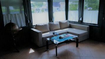 A room with a beige sofa, a glass coffee table, and large windows.